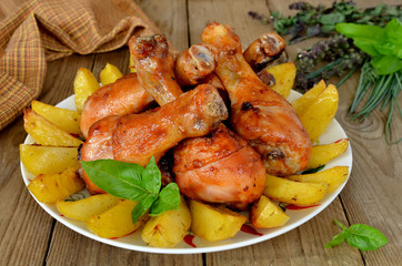 Roasted chicken legs with potatoes in a pan on wooden background
