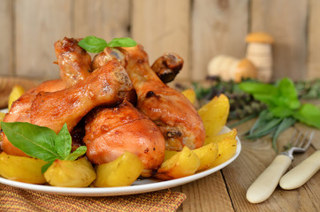 Roasted chicken legs with potatoes in a pan on wooden background