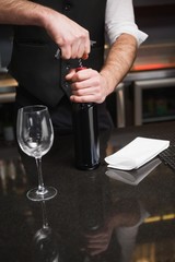 Handsome waiter opening a bottle of red wine