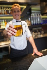Smiling bartender offering pint of beer to camera