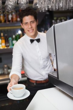 Barista offering cup of coffee smiling at camera