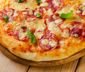 Salami pizza with cheese and basil on a wooden  board.