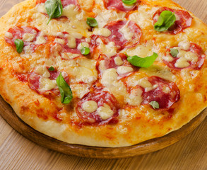 Salami pizza with cheese and basil on    board.