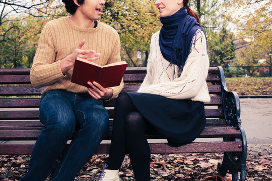 Man Reading For Woman On Park Bench