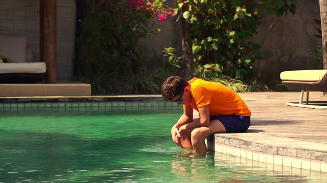 Sad young teenager sitting on the edge of swimming pool