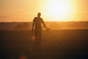 Fotobehang Treasure hunter with Metal detector in the field on the sunset © dislentev