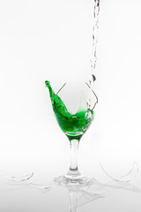 Green water spill from a broken wine glass on white background