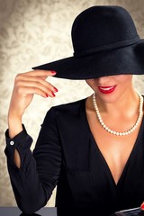 Attractive woman wearing black dress, hat and pearls