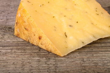piece hard cheese with herbs on an old wooden table