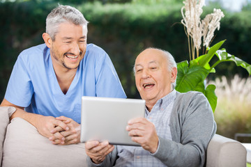 Male Caretaker And Senior Man Using Tablet PC
