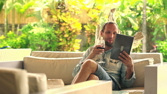 Happy man chatting with friends on a tablet and raising wine toa