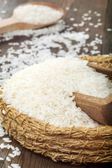 White rice in wicker bowl with wooden spoon on wooden table