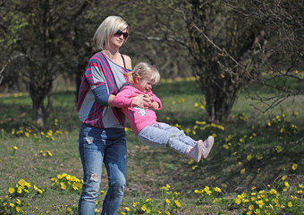 Fototapeta premium Mother and daughter spinning in a park with yellow flowers