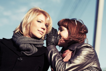 Two happy young fashion women teeling secrets outdoor