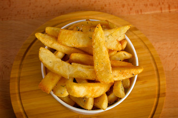 Potatoes fries in a white paper bag on wooden board