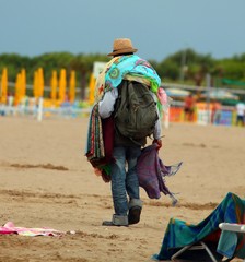 abusive Peddler with fabrics and dresses walking on the beach gl