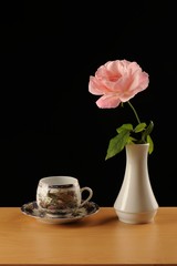Pink rose in white vase and coffe cup isolated black bacground