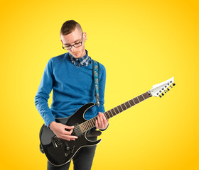 Young man playing guitar over yellow background
