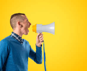 Redhead man shouting by megaphone over yellow background
