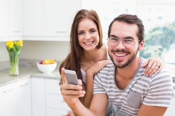 Fototapeta premium Young couple smiling at the camera man holding smartphone