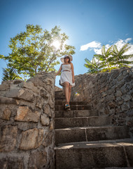 woman in white hat walking down the stone stairs at sunny day