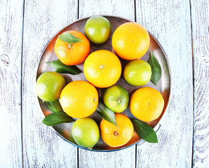 Ripe citrus with green leaves on plate on wooden background