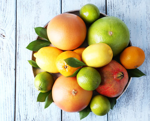 Ripe citrus with green leaves on plate on wooden background