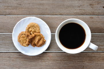 Cookies in white plate and black coffee on wooden table, top vie