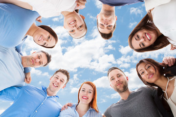 Happy Multiethnic Friends Forming Huddle Against Sky