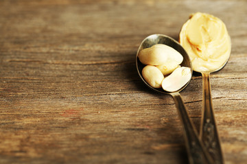 Spoons with fresh peanut butter and nuts, on wooden background