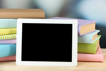 PC tablet and books on wooden table, on light background