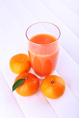 Glass of juice and ripe sweet tangerine on white wooden table