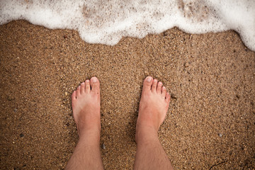 male feet standing on sandy beach