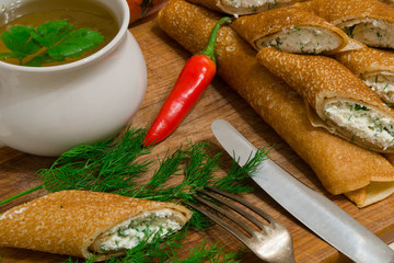 cup of soup and pancakes, rolled on a wooden board with herbs an