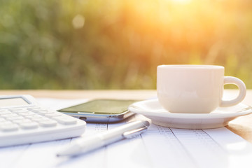 A cup of coffee on the table and calculator with number in paper