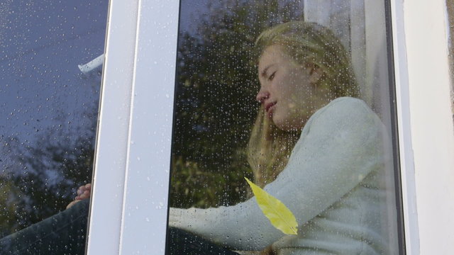 Teenage girl at window crying in the rain
