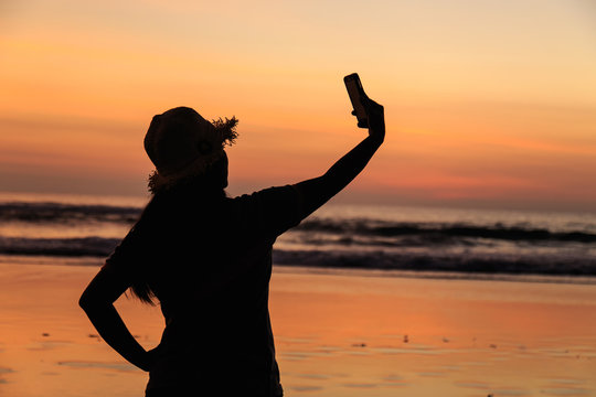 Silhouette of Thai Woman using smartphone at the beach in sunset