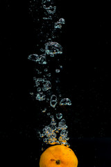 Fresh orange dropped into water with bubbles forming