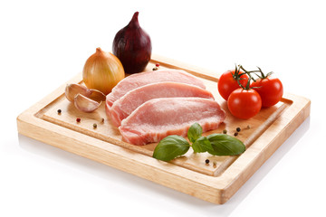 Raw pork chops on cutting board and vegetables