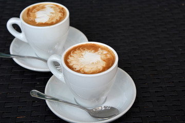 Two cups of hot cappuccino on the black background