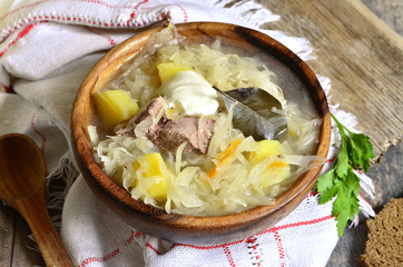 Rustic sour cabbage soup with goose in a wooden bowl.