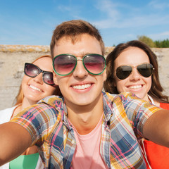 group of smiling friends taking selfie outdoors