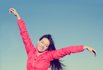 Woman smiling arms raised up to blue sky, celebrating freedom
