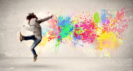 Fototapeten Glücklicher Teenager, der mit buntem Tintenspritzer auf städtischem Hintergrund springt © ra2 studio