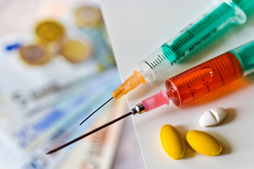 Different pills and syringe with Euro money - healthcare cost co