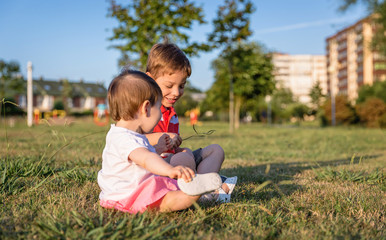 Naklejka na ściany i meble Baby girl and child playing sitting on a grass park