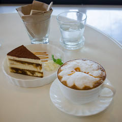 cup of cappuccino in a white cup with tiramisu cake on table