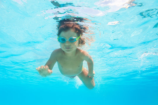 Small boy with goggles swims alone under water