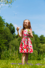 Little girl having fun blowing soap bubbles in park.