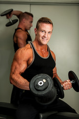 Fototapeta na wymiar Hnadsome young man working out with dumbbells in fitness - powe